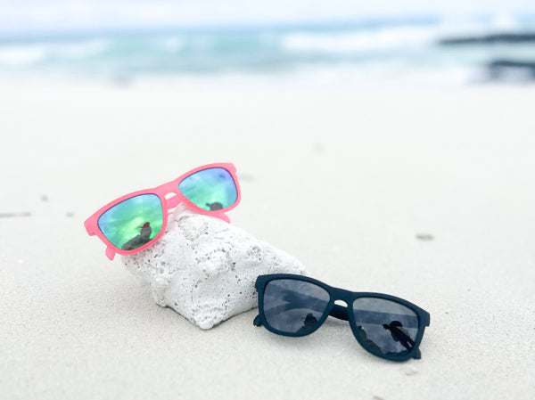 Two BlueBayCo sunglasses lying on a sunny beach